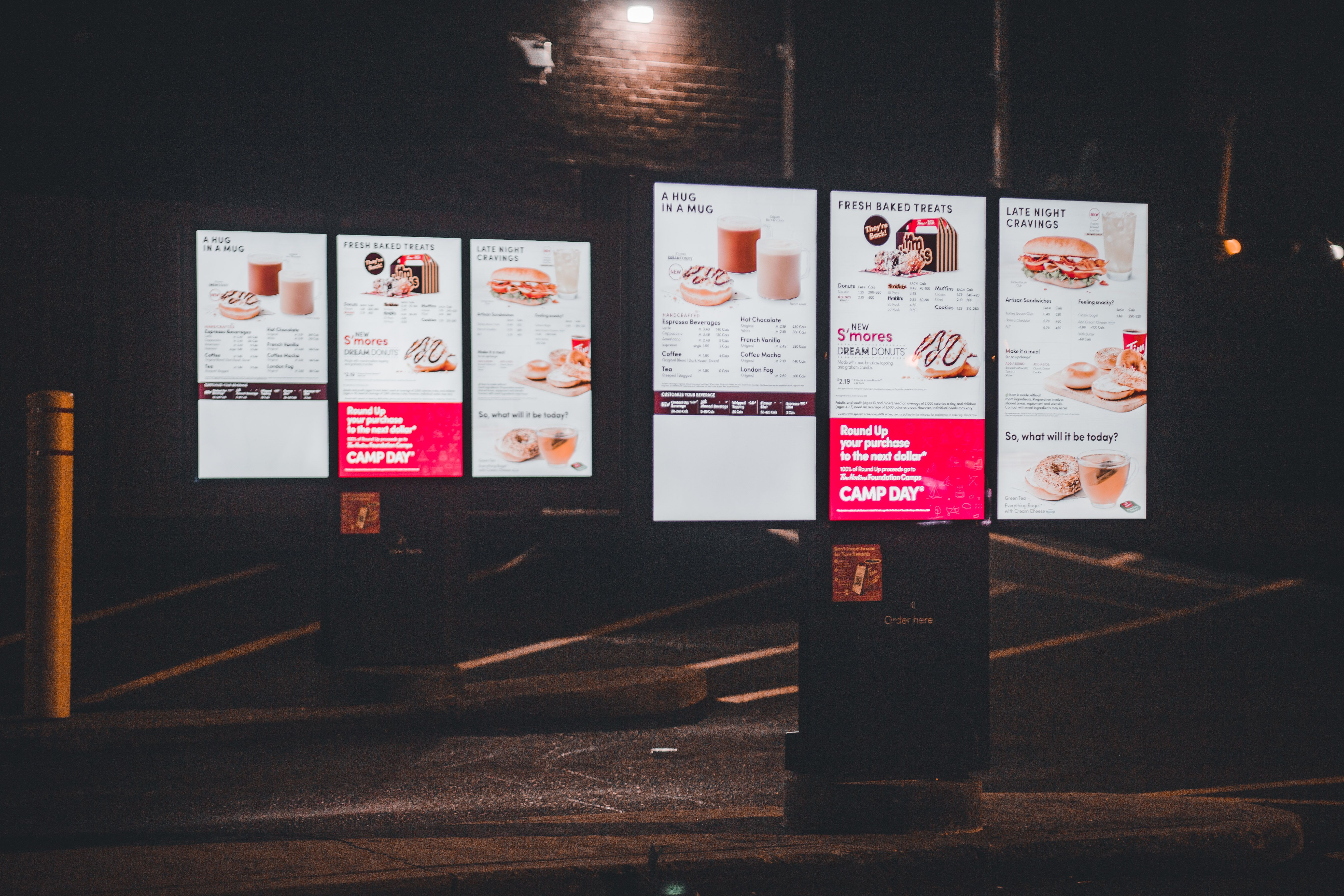 An illuminated digital menu display outside a fast-food restaurant at night.